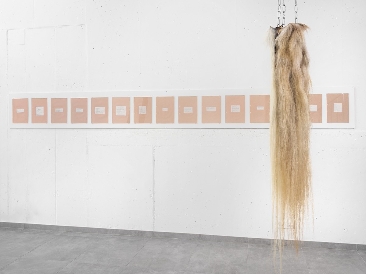 Vue d'exposition avec des oeuvres suspendues par des chaines et des poèmes accrochés au mur