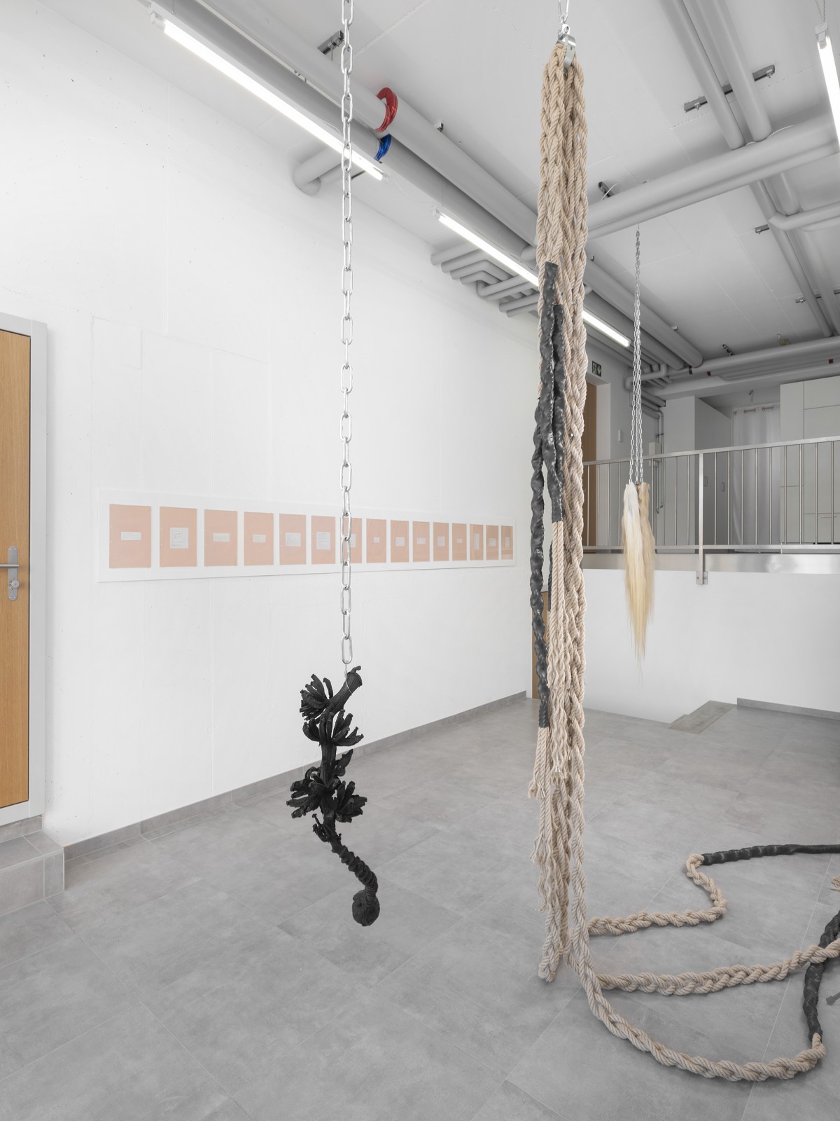Vue d'exposition avec des oeuvres suspendues par des chaines et des poèmes accrochés au mur